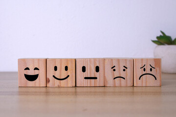 Happy smiling emoticon on top of another emotion faces, stacking wooden blocks. Customer service evaluation, feedback, and satisfaction survey concept. 