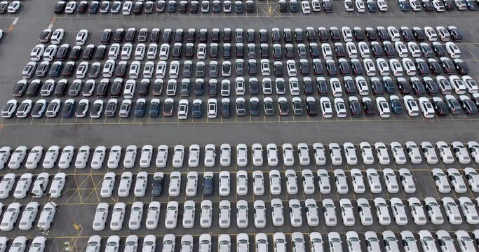 Aerial view of a new car lot, neatly arranged vehicles reflecting uniformity and precision, symbolizing organized commerce and transportation.