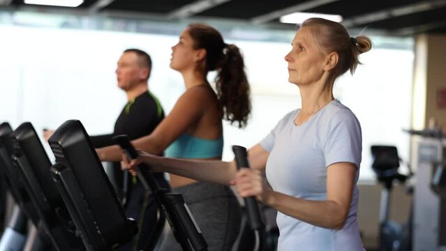 Focused mature woman using elliptical machine in gym 