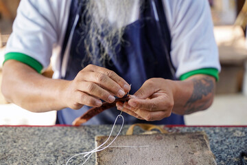 Closeup hands of Asian leather craftsman is carefully to sew a leather belt for a customer.,...
