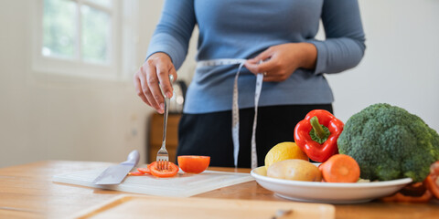 Young woman asian measure her waist in the kitchen the with vegetables and fruits. Concept of...