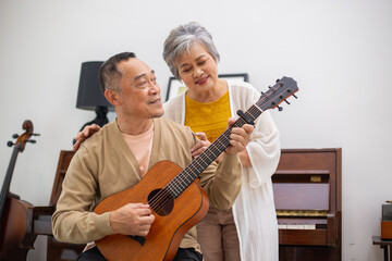 Happy asian senior elderly couple take it easy on retirement holidays playing guitar having fun in...