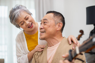 Happy asian senior elderly couple take it easy on retirement holidays playing guitar having fun in...