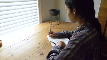 Inspirational young Puerto Rican female writing daily mental health journey in personal journal, Over shoulder view
