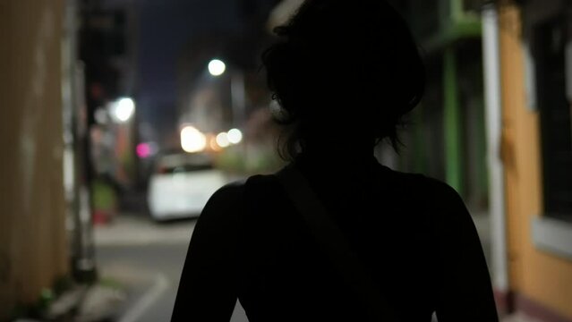 Unrecognizable young girl with solitude walking alone on a dimly lit street at night.