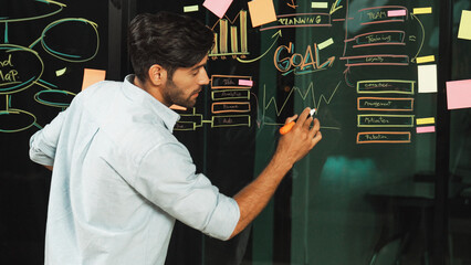 Smart manager writing business plan at glass wall on sticky notes. Skilled businessman sharing,...