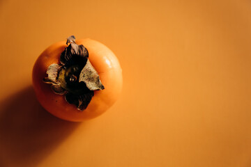 Ripe persimmon on orange background. Minimal concept.
