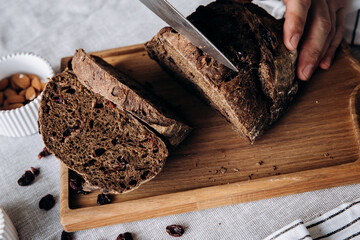 Chef slices fresh bread on a wooden cutting board with raisins and cranberries