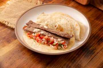 Tacos de Arrachera. Homemade grilled meat in a wheat tortilla. Street food from Mexico, traditionally accompanied with cilantro, onion and spicy sauce or guacamole.