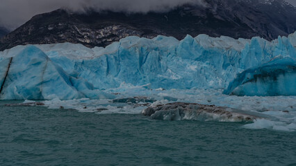 A melting glacier. A wall of blue ice rises above a turquoise glacial lake. Thawed ice floes,...