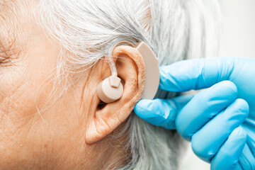 Asian senior woman patient wearing a hearing aid for treating hearing loss problem. - obrazy, fototapety, plakaty