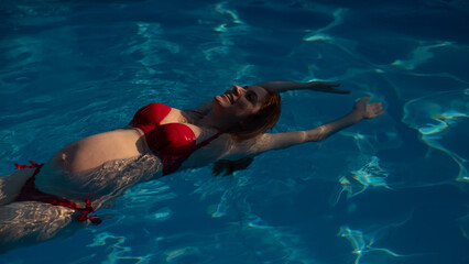 Top view of pregnant woman floating in pool in red bikini. 