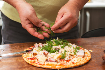 Obraz na płótnie Canvas Sprinkle herbs on pizza. Male hands add dill to pizza.