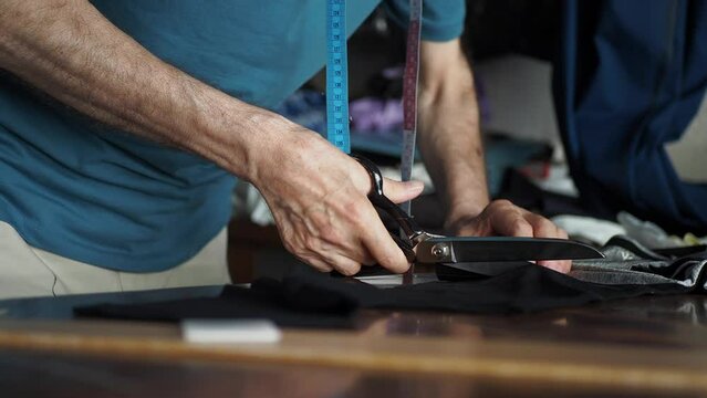 men using scissors to cut piece of fabric 