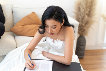 Asian woman in elegant bridal gown completing legal marriage paperwork. Bride in a white dress...