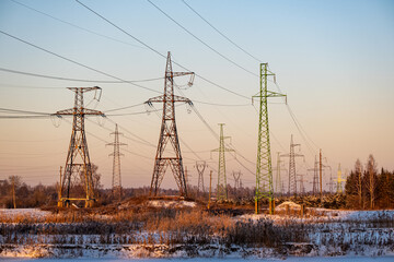 High voltage power lines and pylons on field in winter. Landscape with golden sunset light in cold...