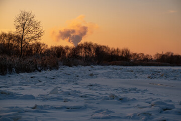 Winter landscape with smoke from the chimney of an industrial plant. Landscape with golden sunset light in cold winter evening in Latvia