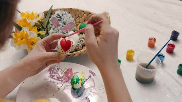Close up of female hands decorating eggs for Easter with red heart shape. Top view from the shoulders. Concept of traditional celebrations and creativity