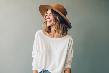 Portrait of a smiling young woman in hat standing against gray wall
