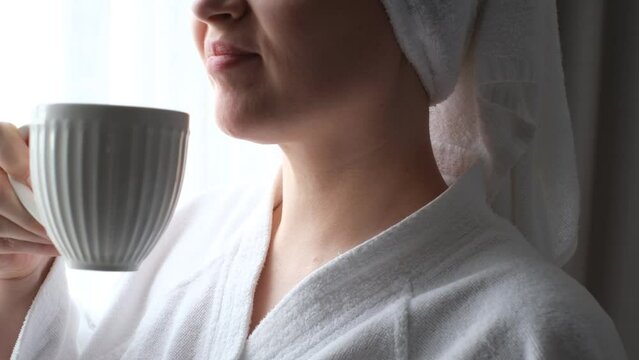 Young woman in white bathrobe drinking coffee side view, concept of vacation.