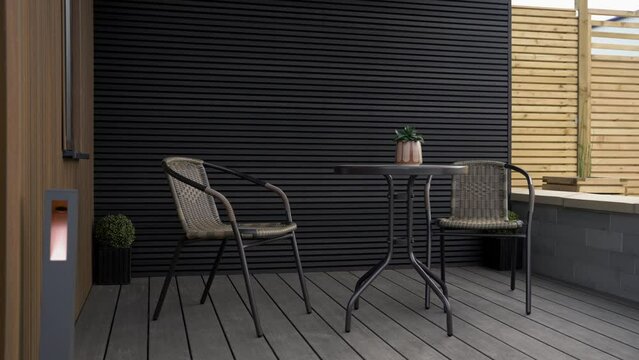 Wide reveal of undercover garden entertaining area with table and chairs surrounded by grey and brown cladding outside of a newly built luxury garden room