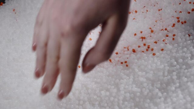 A woman mixes plastic granules with orange pigment to create colored plastic. Polymer composites are used in industry as raw materials for the production of various products
