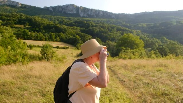 Senior woman photographer taking photos in the mountains on a sunny day