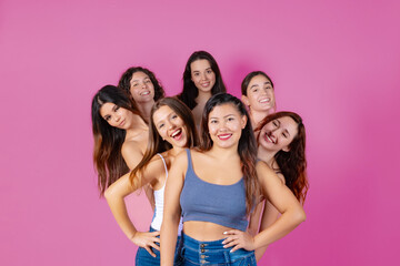 Seven friends sharing joy and happiness, posing playfully on a bright pink background.