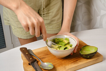 Woman mashes avocado pulp with a fork in a bowl