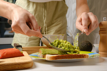Unrecognizable woman spreading mashed avocado on sandwich