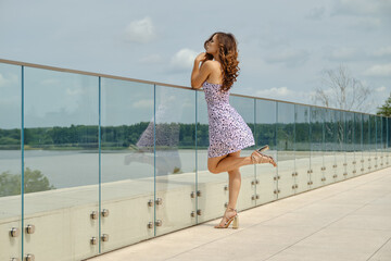 Slender woman in sundress leans on glass railing of observation deck