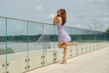 Slender woman in sundress leans on glass railing of observation deck