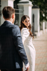 A man and a woman holding hands. The woman is wearing a wedding dress and the man is in a suit. 5116