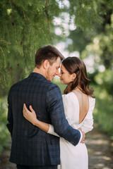 A man and woman kissing outdoors, possibly in a romantic setting. They are both wearing wedding attire, suggesting