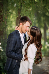 A man and a woman kissing outdoors, possibly at a wedding or another romantic event. They are both...