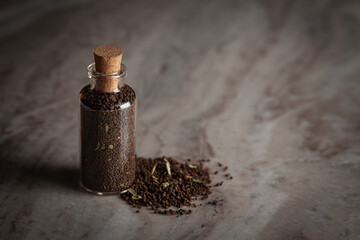 A small glass bottle filled with dry tea leaves. Placed on a marble background.