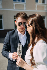 A man and a woman standing outdoors and holding a glass. Both are wearing sunglasses and appear to be smiling. 5176