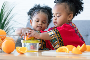 Two African cute kid girls squeezing fresh oranges at home. Adorable children siblings help making freshly squeezed orange juice on manual juicer together. Healthy lifestyle and learning concept - obrazy, fototapety, plakaty