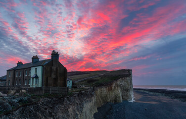 Dramatic dawn sky over the precarious cottages on the cliff edge of Birling Gap on the south downs...