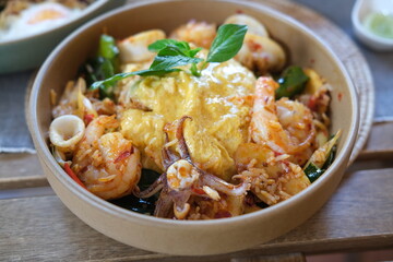 traditional Thai food know as spicy Tom Yum Kung Fried Rice, topped with omelet. Ingredients include galangal, lemongrass, kaffir lime leaves, basil leaves, eggs, chilli, shrimp and squid.