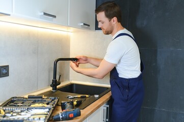 Happy Young Male Plumber Fixing Faucet In Kitchen