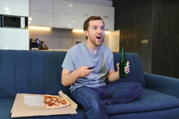 Eats pizza while watching TV show. Man with beard indoors.