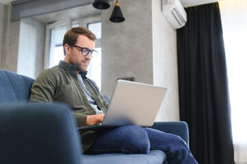 Side view handsome young businessman in eyewear working with computer. Pleasant happy man communicating in social network, searching information online