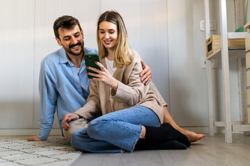 Smiling couple embracing while looking at smartphone. People sharing social media on cellphone.