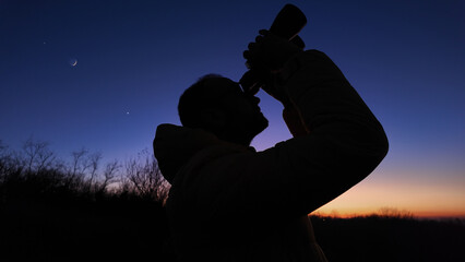 Amateur astronomer looking at the evening skies, observing planets, stars, Moon and other celestial objects with binoculars.