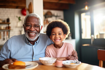Smiling African American grandfather and grandson, senior or old man sitting at table, eating and...