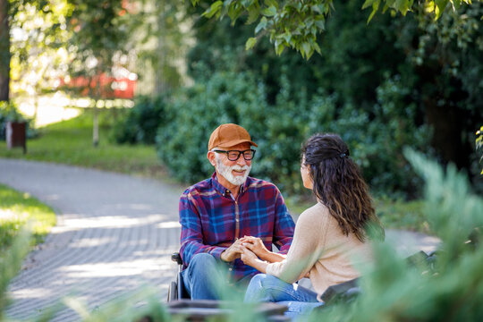 Smiling Retired Senior Man In Wheelchair Holding Hands With Social Worker