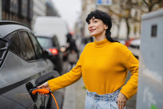 Smiling woman charging electric car at station