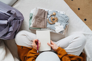 Pregnant woman preparing checklist with diary at home