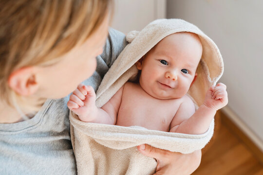 Mother carrying smiling baby son wrapped in towel at home